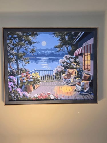 Customer's Custom Paint By Numbers landscape art framed on a wall, depicting a moonlit deck with rocking chairs.