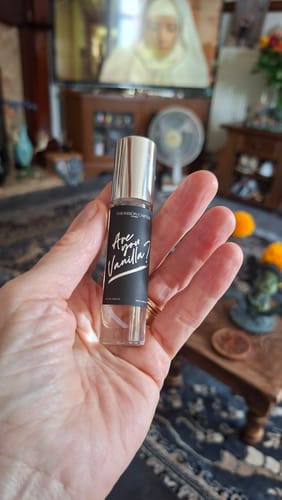 Reviewer's hand holding a cylindrical Are You Vanilla? Night perfume bottle with a black label.