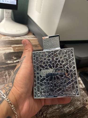 Customer's hand holding the elegant, square Rayhaan Aquatica perfume bottle with ornate silver latticework.