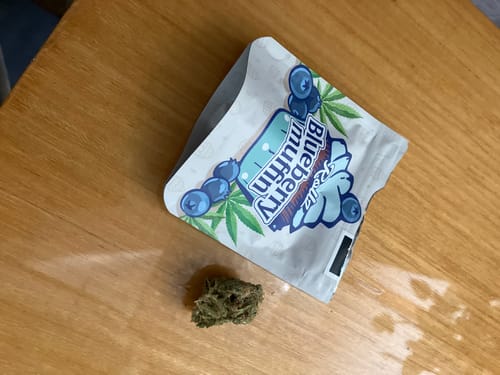 Customer's Rollz Blueberry Muffin THC-A flower bag and a single green bud on a wooden surface.