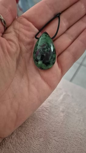 Customer's Pendentif Rubis Zoïsite, a green and dark red drop-shaped stone pendant held in a person's hand.