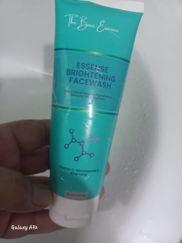 Reviewer's hand holding a turquoise Essense Brightening Facewash tube against a white background.