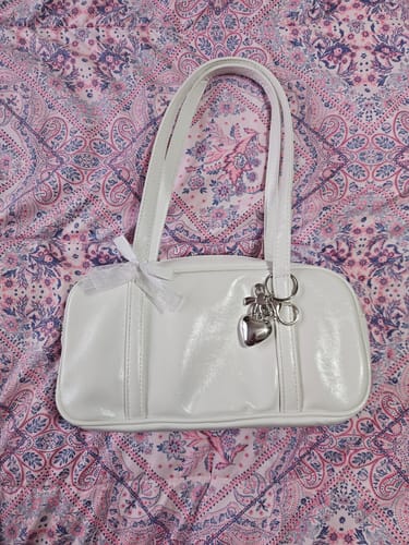 Customer's white Sawako Inspired Bag with a heart charm and bow detail resting on a patterned pink quilt.