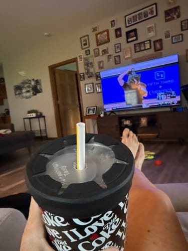 Customer's To-Go Buddy cup holder with Diet Coke branding, held by a hand in a living room while watching television.