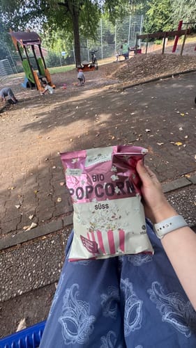 Customer's hand holding a bag of Bio Popcorn Süß from the Heimatgut Probierbox at a playground.