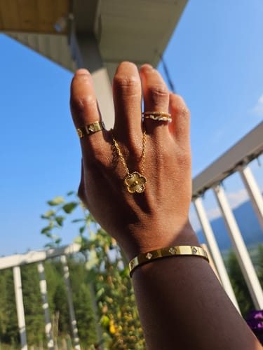 Customer's hand wearing a golden clover necklace and matching accessories against a bright outdoor background.