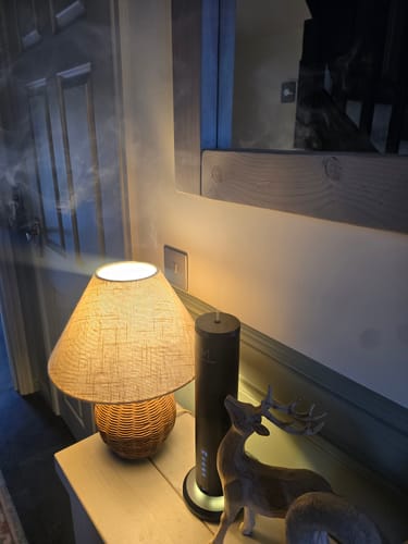 Customer's LumaMax waterless diffuser in black, emitting a light mist on a wooden table beside a lamp.