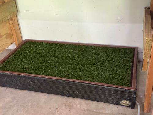 Customer's Porch Potty STANDARD grass unit with dark wicker frame, set on concrete floor in a garage.