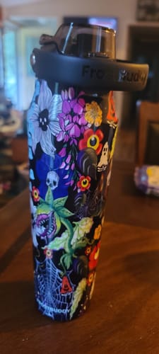 Customer's Bottle Buddy in Toxic Bloom print featuring colorful skulls and flowers, standing on a wooden surface.