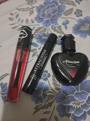 Reviewer's Ativador de Feromônios - Attracione shown with two other dark perfume bottles on a floral patterned surface.