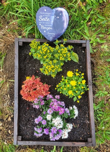Kunden-Foto des Schieferherz-Grabschmucks, platziert in einem bepflanzten Holzkasten im Garten.