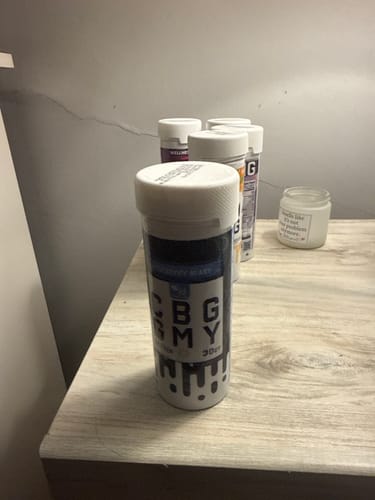 Customer's Blueberry Blast CBG Gummies container on a light wooden surface with other supplement bottles.