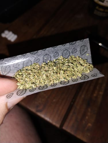 Customer's Zkittlez THCA Flower ground up in a leaf-patterned rolling paper held by a hand.