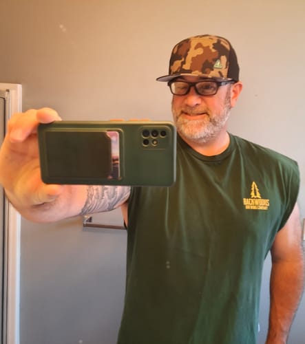Customer's Big Flat Bill Structured Watersport Hat in a camo print worn by a person in a green t-shirt