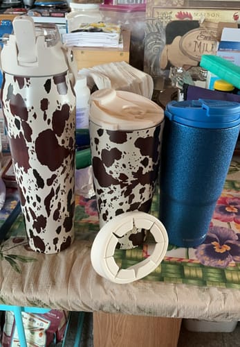 Customer's To-Go Buddy cup insulators in cow print alongside a blue tumbler and a white silicone ring on a table