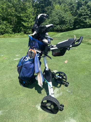 Reviewer's blue Cybercart electric golf caddy holding a golf bag, parked on a green golf course.