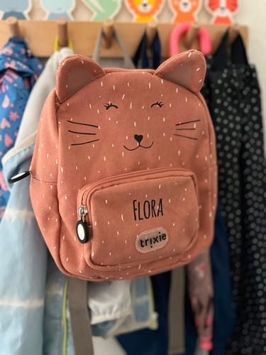 Kundenfoto des personalisierten, altrosafarbenen Trixie Rucksacks in Katzenform mit Namen Flora, hängend an einer Garderobe.