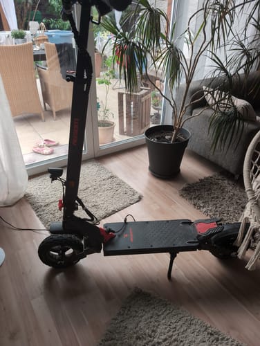 Customer's Ausom L1 Controller electric scooter standing on a living room floor near a houseplant and glass door