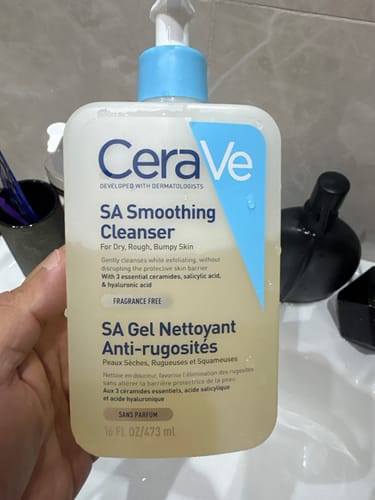 يد المراجع تحمل عبوة غسول CeraVe SA Smoothing Cleanser في حمام