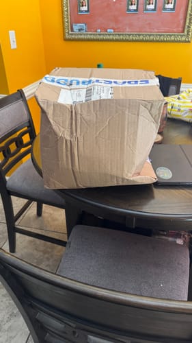 Customer's shipping box for the Universal XL, showing damage to the cardboard while sitting on a round table.