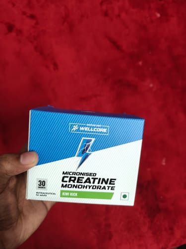 Customer's hand holding a blue and white Wellcore Creatine Monohydrate box against a red background.