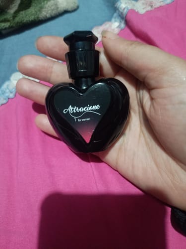 Reviewer's hand holding a small black heart-shaped Attracione perfume bottle.
