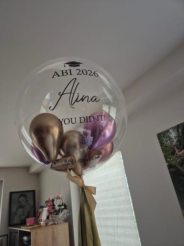 Kunden-Geldbefüllung im transparenten Luftballon mit der Aufschrift ABI 2026 und Alina, befüllt mit glänzenden Ballons.