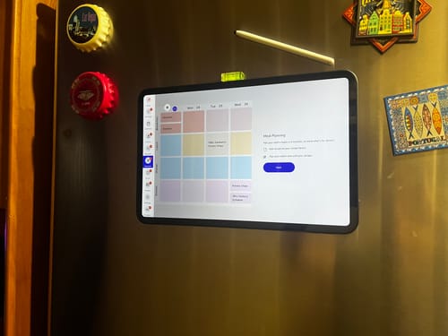 Customer's FridgeCal calendar mounted on a refrigerator, displaying a colorful weekly meal planning interface.