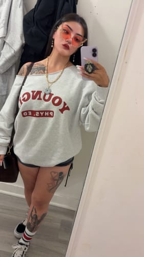 Customer's grey P.E. Crewneck with red branding worn as an oversized shirt while taking a mirror selfie.