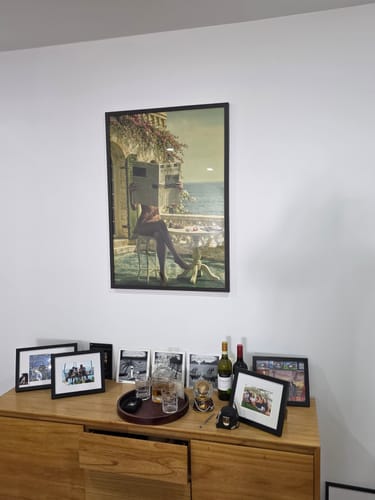 Customer's framed La Dolce Niente N02 art print hanging on a white wall above a wooden cabinet.