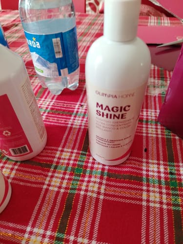 Reviewer's Magic Shine cleaning additive bottle on a red and white checkered tablecloth next to a water bottle.