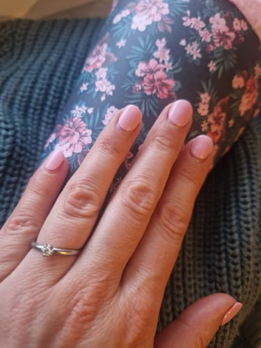 Reviewer's hand wearing pink UV Gel Lovely Pink nail wraps, holding a floral patterned item.