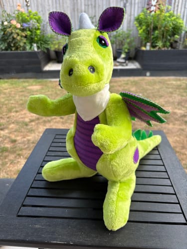 Customer's plush dragon toy made from soft, green fleece fabric, posed on a black table outdoors.