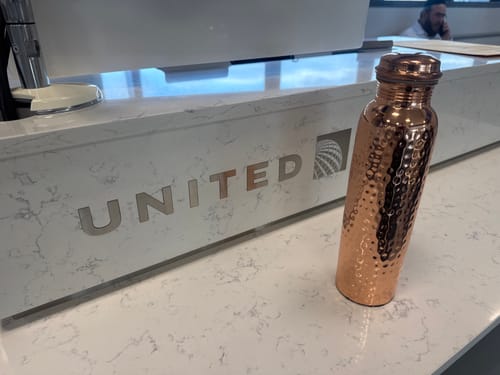 Customer's hand-hammered copper water bottle placed on a white airline check-in counter at the airport.