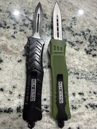 Customer's two VF-1 Black D/A OTF knives, one black and one olive green, displayed open on a speckled surface.