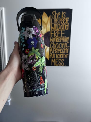 Customer's hand holding the Bottle Buddy in Toxic Bloom print, featuring floral and spiderweb designs.
