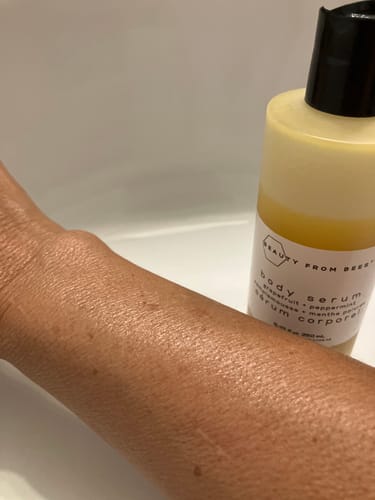 Customer's arm showing hydrated, glowing skin next to a bottle of Body Serum.