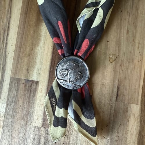 Customer's Firework bandana featuring orange and beige patterns on black, fastened with a silver ring on a wooden surface.