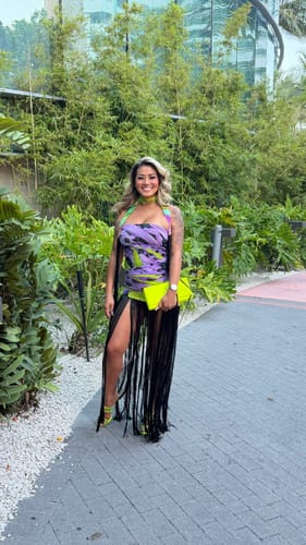 Customer wearing a purple patterned tube dress with long black fringe detailing while standing outdoors.