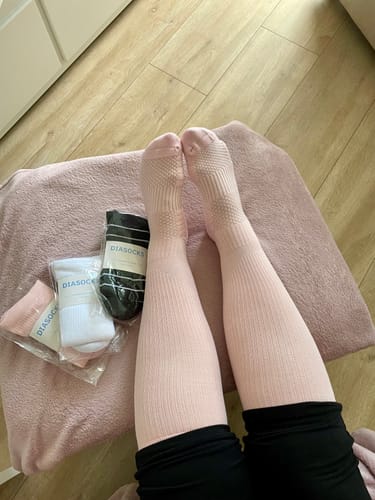 Kundens ben iklädda mjuka, rosa Diasocks stödstrumpor med två paket i bakgrunden