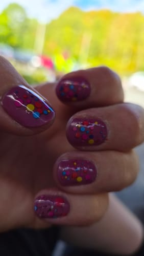 Customer's hand showing nails with smooth purple gel polish and colorful sticker accents.