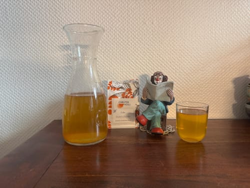 Customer's Durstlöscher Eistee-Packung neben einem Glas und einer Karaffe mit bernsteinfarbenem Tee auf einem Holztisch.
