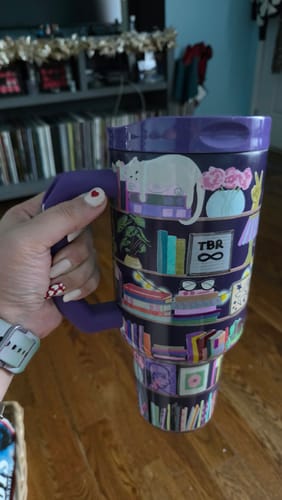 Customer's purple Thicc Buddy mug with illustrated book-themed print held in a hand.