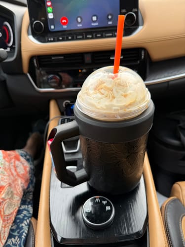 Customer's black Thicc Buddy mug containing an iced coffee with a straw, sitting in a car cup holder.