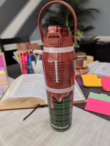 Customer's Bottle Buddy in a football field design, resting on a table with stationary and a book.
