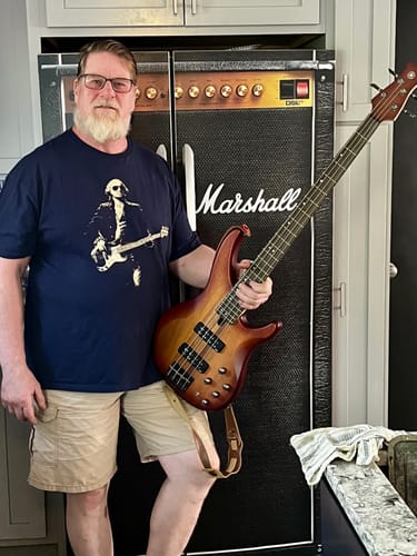 Customer's Washington Bass Face T-Shirt on a person holding a guitar in front of a guitar amp decoration.