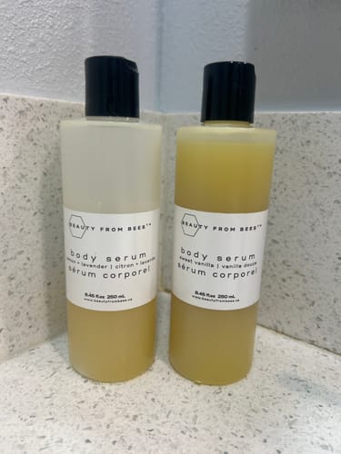 Customer's two bottles of Body Serum sitting on a white speckled bathroom counter.