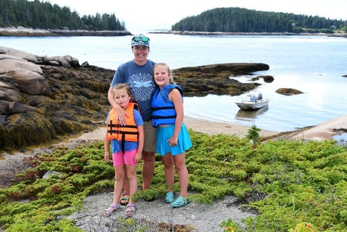 Customer's Dragonfly Thistle T-Shirt worn by a person standing with two children near a coastal beach.