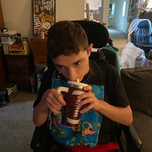 Customer's person using a brown and white CREWCUP tumbler with a handle while sitting in a wheelchair.