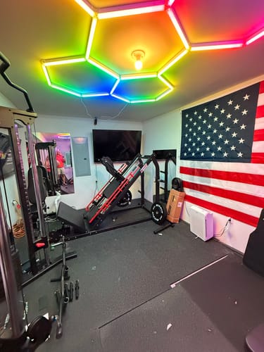 Customer's RitFit PLC01 Leg Extension Machine and leg press equipment setup in a home gym with an American flag on the wall